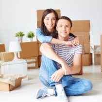 Happy young couple sitting on the floor of new house surrounded by boxes